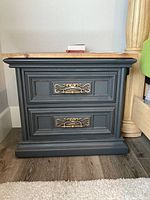 Full front view of the wood nightstand showing dark painted drawers with brass decorative handles and base molding.