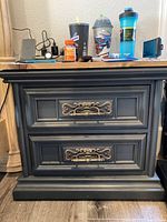 Front view of wood nightstand with two drawers, decorative metal handles, dark finish, and various items on top.