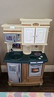 Front view of the play kitchen showing microwave, oven, sink, stovetop and cabinets.
