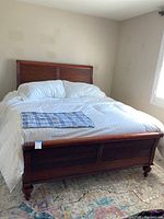 Queen size wooden bed frame with white bedding and king size mattress in bedroom near window with shutters.