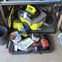 Ryobi cordless wet/dry vacuum with hose and Black & Decker paint sprayer with accessories including spray nozzle and instruction manual.