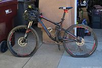 Full side profile view of black and red Trek Fuel EX 8 mountain bike leaning against house wall with helmet on handlebar
