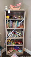 Full view of the wood bookshelf unit filled with various children's books, toys, and decorative items.