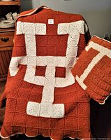 Photo showing the UT pillow resting on the crocheted afghan blanket with the interlocking UT logo in white on burnt orange background.
