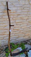 Antique wooden handled scythe with metal blade propped against stone wall, showing full handle and wooden grips.