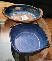 Two blue stoneware serving dishes displayed on a glass table, showing shape and color details