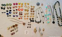 Wide view of a collection of costume jewelry including earrings, necklace sets, and pins laid on a flat surface.