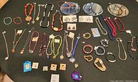 Full overview of costume jewelry pieces including necklaces, bracelets, earrings, and small accessories arranged on black fabric.