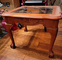 Side angle photo showing wooden table legs, carved apron, and glass-insert top surface on wood