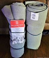 Two rolled gray sun screen fabric pieces, one with a red and white label showing product details.