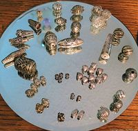 Close-up photo of silver beads, cone-shaped findings, and spacers arranged on a mirror showing reflective double images.