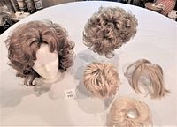 Lot showing two synthetic wigs and three smaller blond ponytail hair pieces arranged on a table.