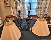 Full view of both table lamps with cream-colored shades on a black tablecloth, showing the matching bases and shades in very good condition.