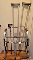 Full set of medical walking aids including walker, cane, and crutches shown against a white door.