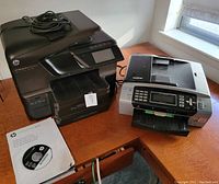 Photo of HP OfficeJet Pro 8600 printer and Brother MFC 490CW printer on a wooden desk with installation disc for HP printer.