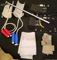 All items laid flat on black fabric background showing sock pulls, back braces, grabber, wrist brace, abdominal brace, and orthopedic wraps.