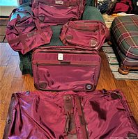 Photo showing all five burgundy soft fabric luggage pieces, including garment bag, large suitcase, two duffel bags, and small pouch.