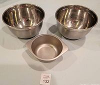 Three stainless steel mixing bowls: Two larger bowls with non-slip bases and one smaller bowl with handle grip, displayed on table surface.
