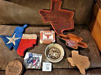 Image of Texas-themed items including a red wire basket shaped like Texas, three sets of coasters, cactus shaped salsa bowl, cork ashtray, fabric patch, and potholder.