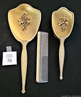 Front view of the dresser set showing hand mirror, comb, and hairbrush with detailed raised gold floral motifs and decorative handles.