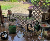 Photo of white wooden lattice panels, semi-circular metal plant stands, various plant pots, standing bird bath, and decorative yard items on a patio.