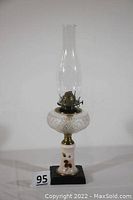 Full view of antique kerosene oil lamp showing the clear glass chimney, brass burner, cut glass reservoir, hand-painted milk glass base with white rose design and black stand below.