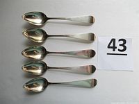 Top view of five silver teaspoons aligned with monogram 'RSW' visible at the handles, next to a paper with number 43