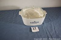 Full view of Corning Ware Blue Cornflower 4-quart casserole with clear glass lid on blue fabric surface.