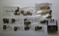 Multiple small plastic bags labeled by country containing foreign coins mostly from European countries and Allied Military Currency from 1943. Includes an old steel razor box with coins inside.