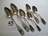 Six coin silver spoons displayed side by side showing variation in size and handle design.
