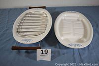 Two Corning Ware Blue Cornflower P19 platters shown side by side; left is three-piece set with metal cradle and rack, right is a matching single platter