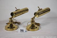 Front view of two matching brass portable desk lamps, showing cylindrical ventilated shades and round bases with power cords.