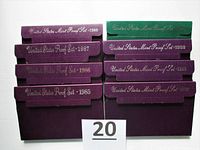 Eight envelopes containing U.S. Mint Proof Sets from 1985 through 1994 with the exception of 1988 and 1990 missing. Purple and green cardboard packaging showing years and United States Mint Proof Set text.