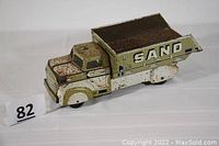 Full view of the vintage tin dump truck showing cream and brown paint and rust spots.