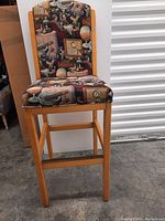 Front view of a single bar chair showing detailed printed upholstery with vintage graphics and wooden legs.