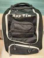 Front view of the black Hap Tim baby carry all bag showing multiple zippered pockets and 'Hap Tim' branding.