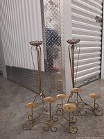 Two brass candle holders side by side. One is tall with a single platform and decorative open scroll rim, tripod leg base. The other is a short horizontal stand with five round candle holders on scrollwork base.