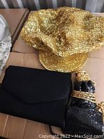 Gold sequin cap, two black bags including one with gold chain and sequin detail on a cardboard surface