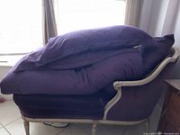 Side view of purple velvet chaise lounge with loose cushions on top, showing carved wooden frame and legs.