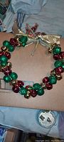 Photo of a circular holiday wreath made of alternating red and green jingle bells strung together with gold ribbon and bow on top, suitable for door decoration.