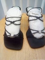 Front view of black strappy women's dress shoes with square toe and rhinestone cluster detail, stuffed with paper to maintain shape.