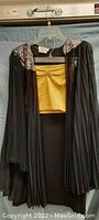 Front view of fan blouse hanging on hanger showing pleated sleeves and gold tube tooth decoration on shoulders