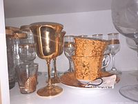 View of two gold-tone metal goblets with polished finish along with two gold-patterned teacups stacked on a matching gold-patterned saucer.