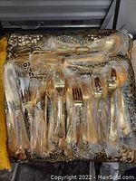 Set of 12 pieces of gold plated silverware, individually wrapped in plastic, displayed on patterned fabric.