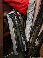 Folded outdoor lounge chair showing wrought iron frame and thick gray cushions with black strapping.