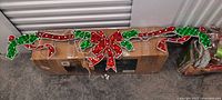 Two long outdoor garland decorations with red bows and holly leaves resting on a box.