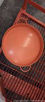 Photo showing large round orange picnic tray with handles placed on a red wire rack.