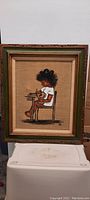 Photo shows framed painting of a child sitting on a chair, the child is playing with a toy. The frame is wooden with a green inner border.