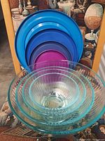View of the set of four clear glass mixing bowls in graduated sizes stacked inside each other, with four colorful plastic lids behind them.