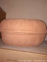 Full side view of the beige clay Romertopf cooking pot with embossed lid showing decorative motifs.